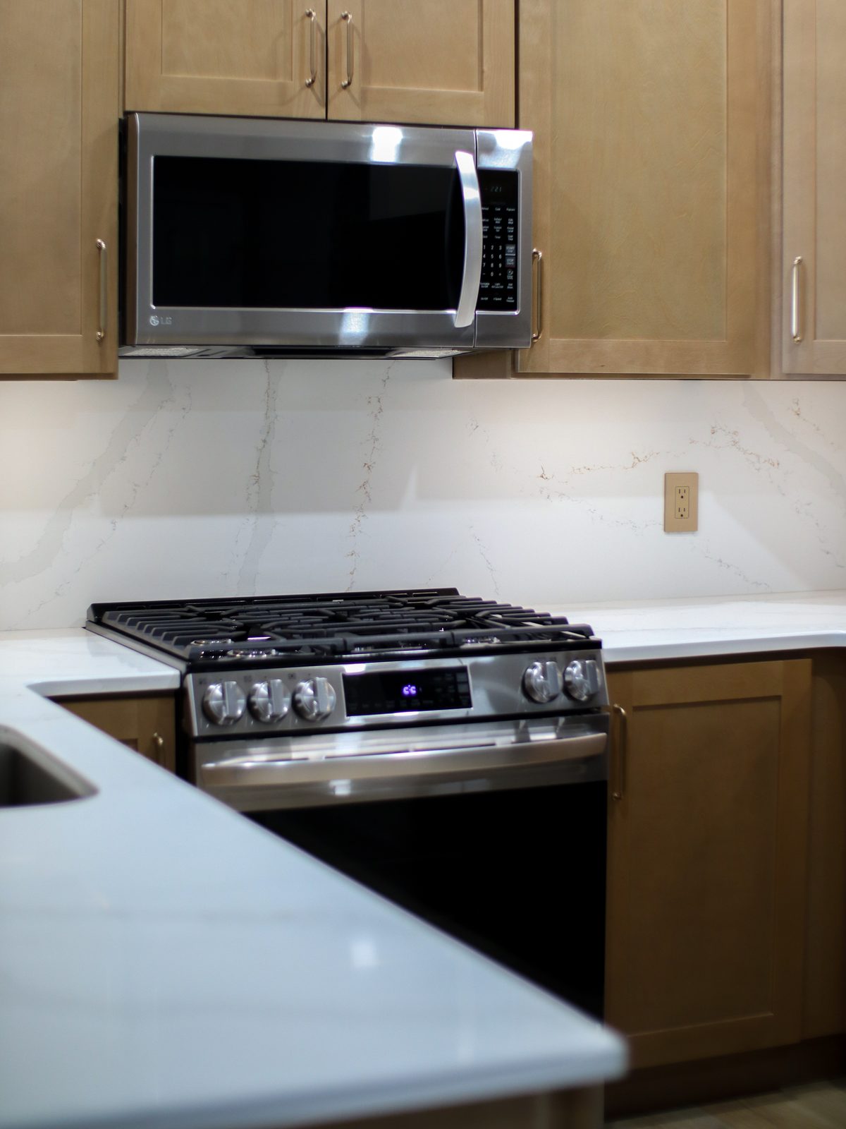 Stainless gas range under the microwave with a quartz slab backsplash