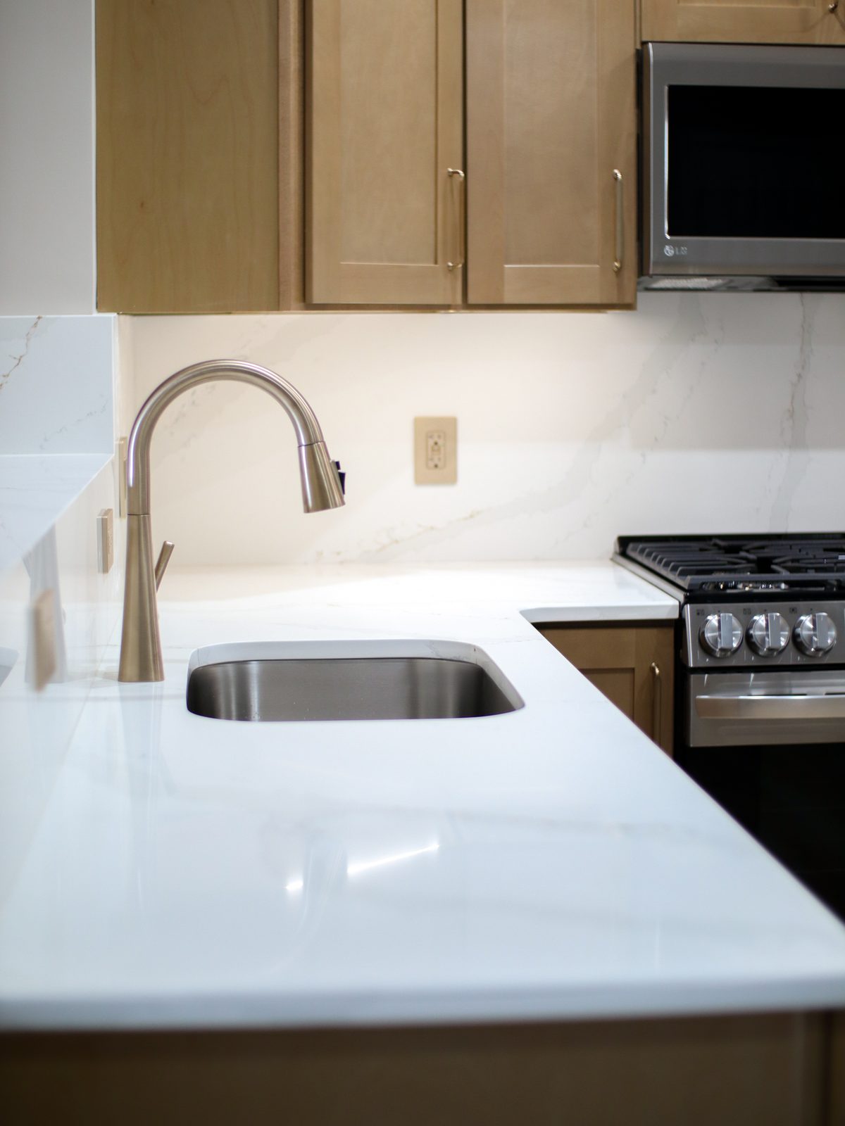 Undermount sink with a gold pull-down faucet and white quartz counters